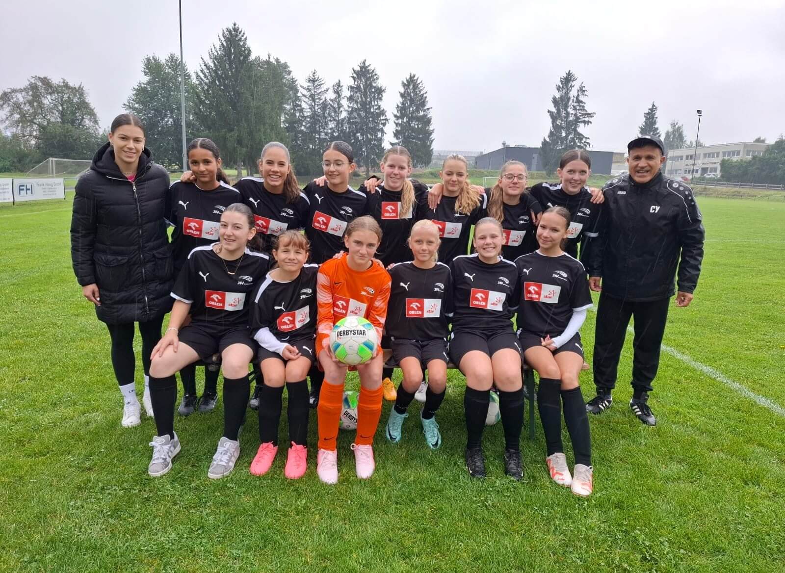 Mädchenfußballmannschaft lächelt und posiert gemeinsam für ein Gruppenfoto auf dem Sportplatz.