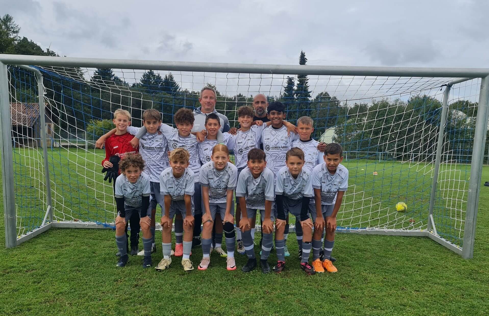 Eine Gruppe von Jungen und Mädchen in Fußballtrikots posiert lächelnd für ein Gruppenfoto.