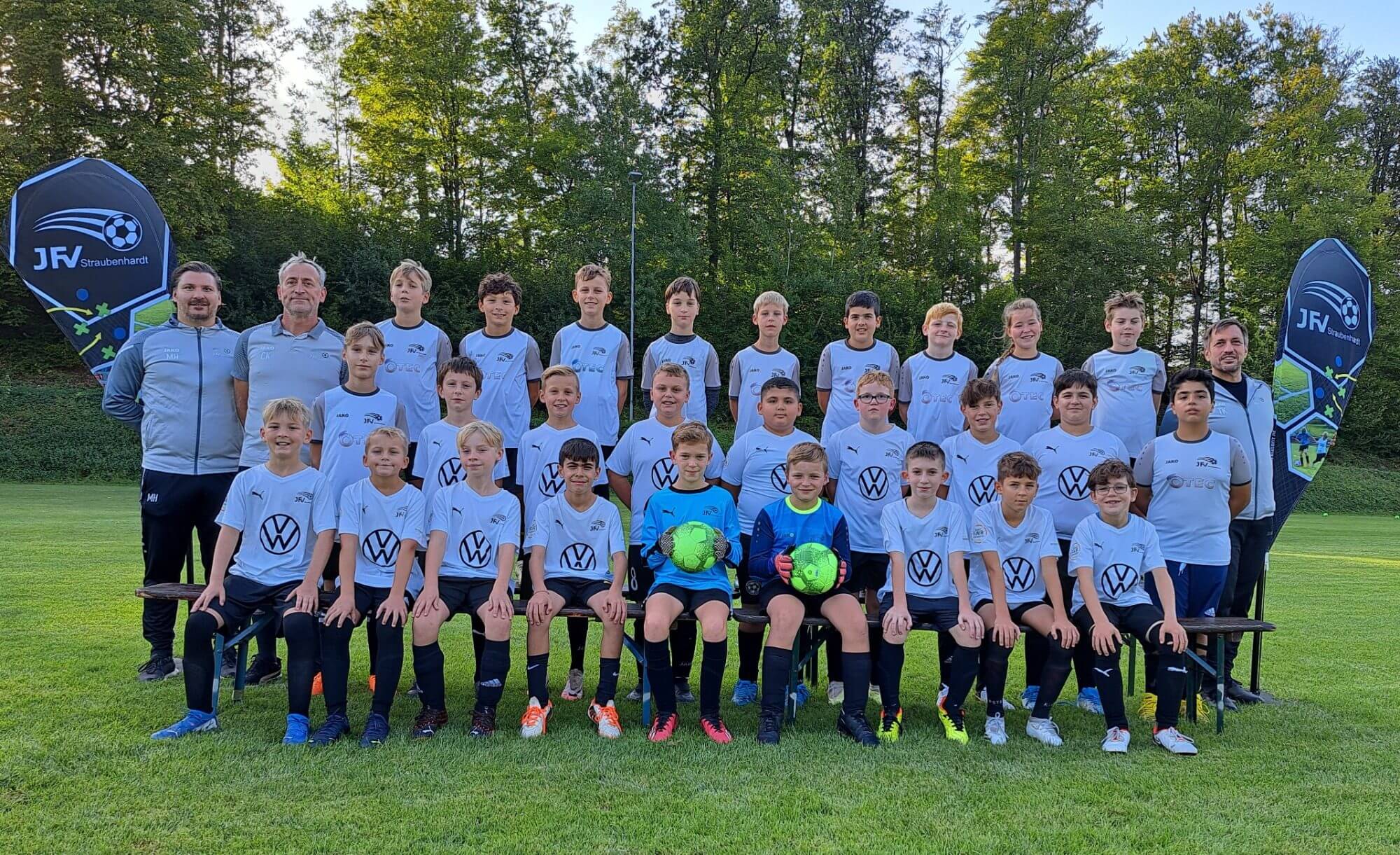 Mannschaftsfoto einer Fußballmannschaft mit Spielern und Trainern, alle in einheitlichen Trikots, lächelnd in die Kamera.