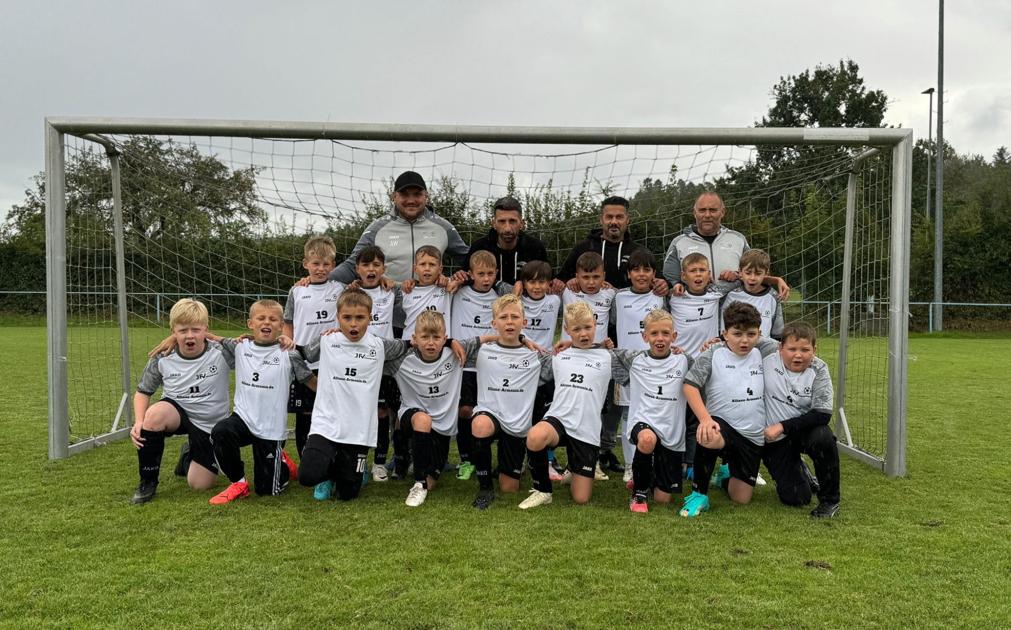 Fußballteam steht lächelnd vor einem Tor für ein Gruppenfoto.